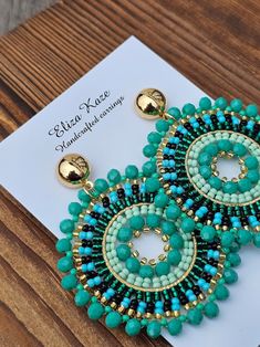 a pair of blue and green beaded earrings sitting on top of a piece of paper