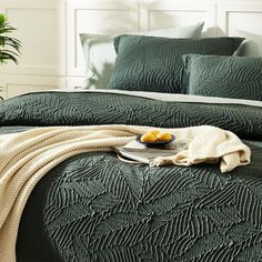 a bed with green bedspread and pillows in a bedroom next to a potted plant