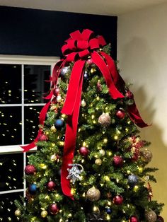 a decorated christmas tree in front of a window with a red bow on it's top