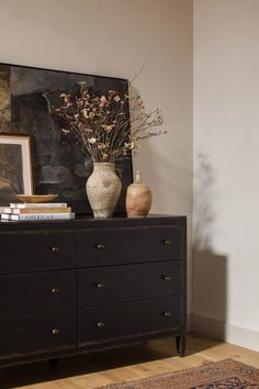 a vase with flowers on top of a dresser next to a painting and framed pictures