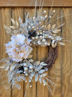 a wreath with white flowers and silver leaves on a wooden door hanger in front of a wood paneled wall