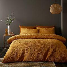 a bed with yellow comforter and pillows in a room next to a lamp on a table