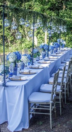 a long table is set with blue and white flowers, plates and umbrellas for an outdoor event