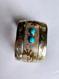 Native American Sterling Silver with 1/20 12GF accents and two small turquoise stones. This bracelet is in good previously owned vintage condition with some sigs of age, wear and tarnishing. There appears to be some loss of the 12k GF finish on the Kokopelli accents. Cuff measures approximately 5 3/4" from one edge of the opening to the other edge of the opening measuring from the interior side of the band. The gap in the cuff to slip your wrist through measure approximately 1 1/8" making the to Turquoise Stamped Cuff Bangle Bracelet, Turquoise Stamped Cuff Bracelet Bangle, Turquoise Stamped Cuff Bracelet Collectible, Traditional Stamped Turquoise Jewelry, Antique Turquoise Bangle Cuff Bracelet, Turquoise Stamped Bangle, Vintage Turquoise Bracelets With Inlay, Vintage Turquoise Bracelet With Inlay, Vintage Turquoise Bangle Cuff Bracelet