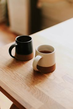 two coffee mugs sitting on top of a wooden table next to eachother