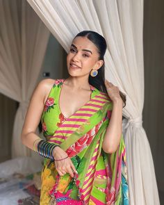 a woman standing in front of a bed wearing a green and pink sari with flowers on it