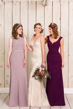 three bridesmaids standing in front of a wooden wall wearing different colored gowns