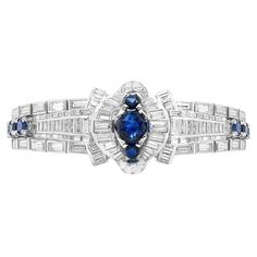 Dating back to the 1950's, this magnificent handmade bracelet features a large royal blue sapphire in the centre, weighing approximately 3.10 carats, set in-between two smaller sapphires inside a halo of channel set diamonds. The bracelet is further decorated with 24 round cut sapphires, set in a panel across the bracelet bringing the total approximate sapphire weight to 14.50 carats. The bracelet is further set with a collection of baguette cut diamonds in both rub-over and channel settings, and pavé set round brilliant in open back settings, totalling to an approximate diamond weight of 25.00 carats. This incredible bracelet measures 7.2 inches in length by 1 inch at its widest point and weighs 73g. Viewed from the side, this bracelet has a diaphanous 3D design turning it into a spectacu River Jewelry, Wedding Jewellery Designs, Platinum Bracelet, Tiffany Bracelets, Retro Bracelet, Art Deco Bracelet, Vintage Sapphire, Style Deco, Bracelet Gemstone