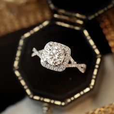 a diamond engagement ring sitting on top of a black velvet box with gold chains around it