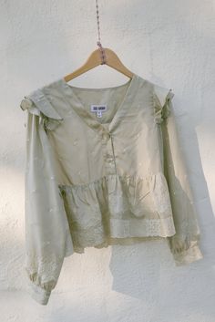 This grey textile is a deadstock silk we found in Los Angeles, CA. It is a light greyish tan color with fine off-white embroidery throughout. The Lupine Top is a long sleeve blouse that drapes around the bust and waist with a ruffle throughout. Features a two-button front and buttons at the cuff. We love this special and relaxed piece. Measurements: Top is measuring flat: Small: Suggested Size 2-4 Bust: 20" (40" total) Waist: Ruffle opens to 30" flat Shoulder: 14" Length: 19" Sleeve Length: 22.5 Off-white Long Sleeve Blouse For Fall, Feminine Neutral Long Sleeve Tops, Off White Long Sleeve Blouse For Fall, Embroidered Long Sleeve Cream Blouse, Fall Wedding Blouse With Long Sleeves, Fall Wedding Long Sleeve Blouse, Silk Long Sleeve Tops With Floral Embroidery, Spring Long Sleeve Beige Blouse, Beige Silk Blouse For Fall