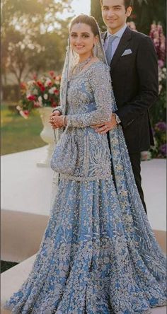 two people standing next to each other wearing blue dresses and tuxedos with flowers in the background