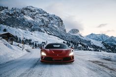 a red sports car driving down a snow covered road in front of some snowy mountains