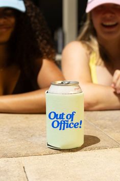 two women sitting at a table with a can of out of office beer on it