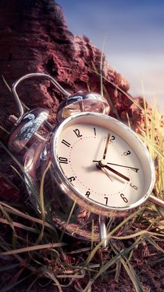 an alarm clock sitting in the middle of some grass and dirt with mountains in the background