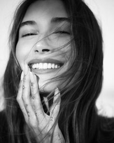 a woman with long hair smiling and holding her hands up to her face as if she were laughing