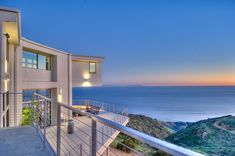 a balcony overlooking the ocean at dusk with stairs leading up to an upper level deck