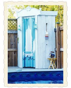 an outdoor shower with blue curtains next to a swimming pool and fenced in area