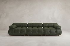 a green couch sitting on top of a white floor next to a gray wall with no one in it