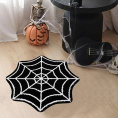 a black and white spider web rug on the floor next to a guitar, skeleton head and pumpkins