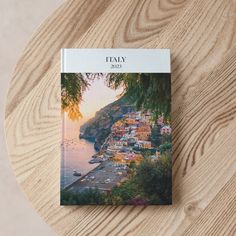 a book sitting on top of a wooden table next to a tree covered hillside and ocean