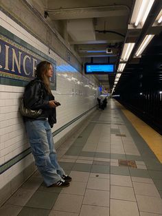 a woman leaning against a wall while looking at her cell phone in a subway station