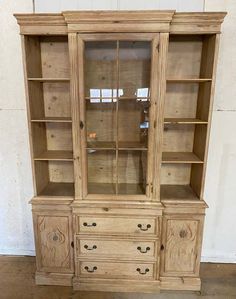 an old wooden china cabinet with glass doors and drawers on the bottom, in front of a white wall