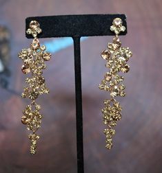 a pair of gold colored earrings sitting on top of a black stand in front of a wooden