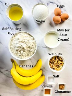 ingredients to make banana bread laid out on a marble counter top, including bananas, flour, eggs, milk, sugar and butter