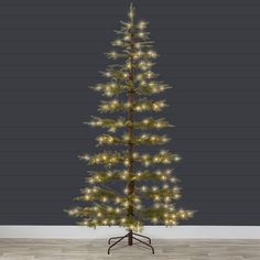 a small christmas tree with lights on it in front of a gray wall and wooden floor