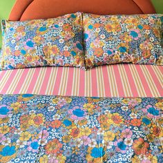 an orange headboard is next to a bed with colorful floral sheets and pillow cases