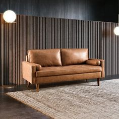 a brown leather couch sitting on top of a rug in front of a wooden wall