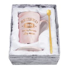 a pink coffee mug in a gift box with a gold spoon and fork on it