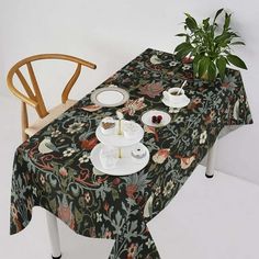 the table is set with tea cups and saucers on it, next to a potted plant