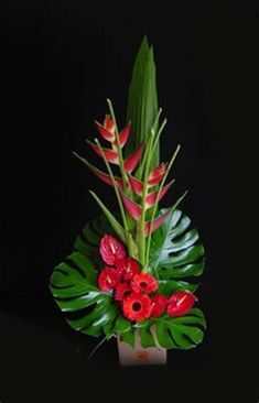 a bouquet of red flowers and green leaves in a square vase on a black background