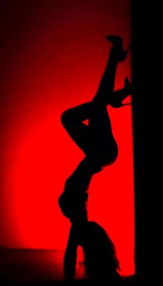 the silhouette of a woman on a pole in front of a red wall with her leg up