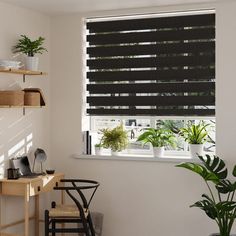 a room with a desk, chair and window covered in black blinds next to a potted plant