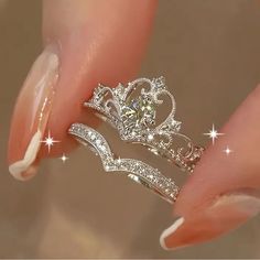 a woman's hand holding two rings with diamonds on them and the middle one has a tiara