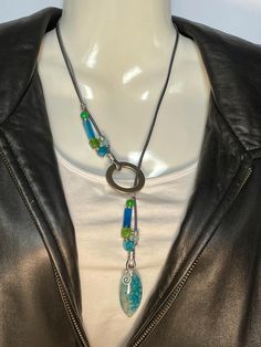 Brilliant Turquoise Dragon's Vein Agate pendant in Lariat or "Y" style necklace. Chrysocolla, Blue Sky Agate, Peridot Agate, Blue Stripe Agate, and Silver Alloy on two strands of leather. A 2mm Gunmetal Gray, and a 1mm Silver cord. Necklace is 22" long, pendant is 1 1/2" x 3/4" and alloy ring is 1 1/4" around. Small Vortex char can be deleted or removed. To wear place open necklace around neck, then put pendant thru ring and adjust as you wish. No lead or nickel used. Please use the Last On, First Off approach. Stones discolor with lotions, perfumes, hairspray, sweat, chlorine, even some soaps, and will break if dropped. Multicolor Adjustable Lariat Necklace, Adjustable Lariat Necklace With Colorful Beads For Gift, Adjustable Multicolor Lariat Necklace With Colorful Beads, Adjustable Green Lariat Necklace, Artisan Turquoise Lariat Necklace Adjustable, Artisan Turquoise Adjustable Lariat Necklace, Turquoise Lariat Necklace Gift, Turquoise Lariat Necklace As A Gift, Colorful Beads Lariat Necklace Gift