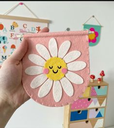 a hand holding up a pink and white flower with a yellow smiley face on it