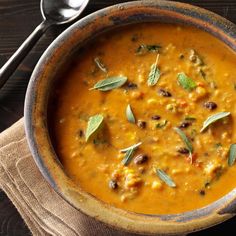 a brown bowl filled with soup on top of a wooden table next to a spoon