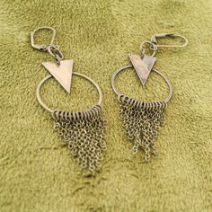 These fun geometric charm earrings come in a subtle antique brass finish. Each earring has a cascade of dainty chains hanging from a hoop in a chainmail reminiscent pattern. These bold and lively earrings are sure to make an impression. With a matching necklace available, this would make a fabulous gift set! -Geometric triangle and hoop charm -hanging chain accents -Antique brass finish -Leverback earring closure Bronze Nickel-free Chandelier Earrings In Brass, Bronze Nickel-free Brass Chandelier Earrings, Vintage Brass Dangle Hoop Earrings, Minimalist Metal Dangle Chandelier Earrings, Bronze Metal Dangle Chandelier Earrings, Bohemian Triangle Nickel-free Earrings, Nickel-free Triangle Bohemian Jewelry, Handmade Triangle Brass Jewelry, Bohemian Triangle Nickel-free Jewelry