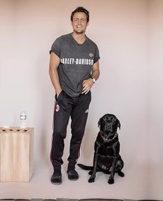 a man standing next to a black dog in front of a white wall with an advertisement on it