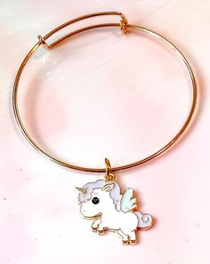 The Pastel Unicorn Gold Bangle Enamel Charm Bracelet is a whimsical and delightful piece of jewelry that adds a touch of magic to your wrist. Crafted with attention to detail, this bracelet features a slim and elegant gold bangle adorned with a enchanting pastel unicorn charm. The charm is beautifully designed with colorful enamel detailing, creating a vibrant and playful look. The bangle is adjustable to fit different wrist sizes, ensuring a comfortable and secure fit. This bracelet is perfect Unicorn Charm Bracelet, Cute Gold Bangle Jewelry, Kawaii Gold Nickel-free Jewelry, Kawaii Nickel-free Gold Jewelry, Gold Nickel-free Kawaii Jewelry, Cute Gold Bracelets For Best Friend Gift, Whimsical Gold Charm Bracelet, White Unicorn Print Jewelry For Gifts, White Unicorn Print Jewelry For Gift