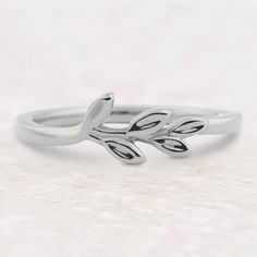 a silver ring with two leaves on the front and one leaf on the back, sitting on a white surface