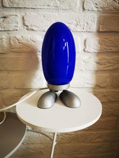 a blue egg sitting on top of a white table next to a brick wall in a room