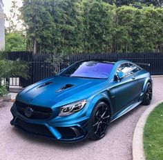 a blue mercedes sports car parked in front of a black fence and green trees behind it