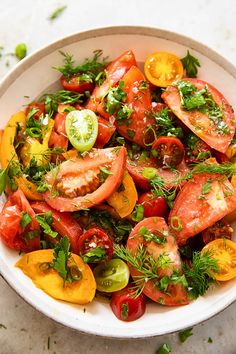 a white bowl filled with lots of different types of tomatoes and green garnish