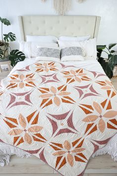 a white bed with an orange and pink quilt on it's headboard next to a potted plant