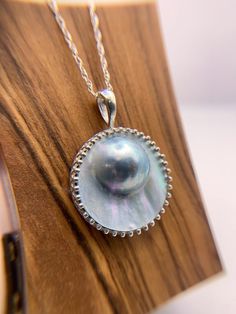 This exquisite necklace showcases a lustrous Mabe pearl of remarkable proportions, measuring a stunning 20 mm in width and rising majestically 8mm above the sterling silver setting. The focal point of this pendant is the remarkable Mabe pearl, boasting a smooth, round surface that radiates a captivating luster, capturing the essence of natural beauty. Nestled within a meticulously crafted regency-inspired bezel setting, the pearl is showcased in all its glory, echoing the opulence of 19th-centur Silver Jewelry With Cabochon Round Beads, Classic Round Tahitian Pearl Necklaces, Classic Tahitian Pearl Round Necklaces, Luxury Silver Pearl Pendant Jewelry, Anniversary Pearl Pendant Necklace In Mother Of Pearl, Anniversary Necklace With Pearl Pendant In Mother Of Pearl, Anniversary Necklace With Mother Of Pearl Pendant, Formal Tahitian Pearl Necklace With Round Pendant, Silver Medallion Jewelry With Pearl Chain