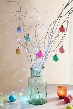 a vase filled with branches and ornaments on top of a table next to a candle